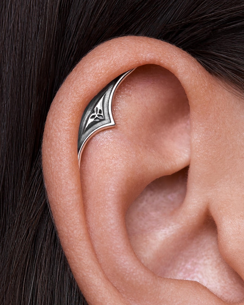 May include: A silver ear cuff with a Celtic knot design. The cuff is curved and has a pointed end.
