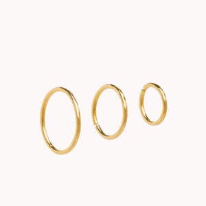 May include: Three gold hoop earrings of different sizes. The hoops are smooth and have a shiny finish.