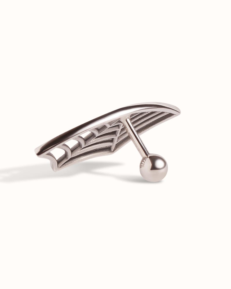 May include: A silver-toned metal body jewellery piece featuring a curved, fan-like shape with an openwork spider web design. The piece includes a straight post attached to the back, ending in a small, smooth, spherical ball closure.