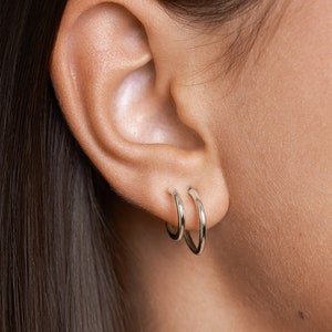 Puede incluir: Primer plano de una oreja con dos pendientes de aro de plata. Los pendientes son de diferentes tama&ntilde;os, el m&aacute;s grande est&aacute; encima del m&aacute;s peque&ntilde;o.