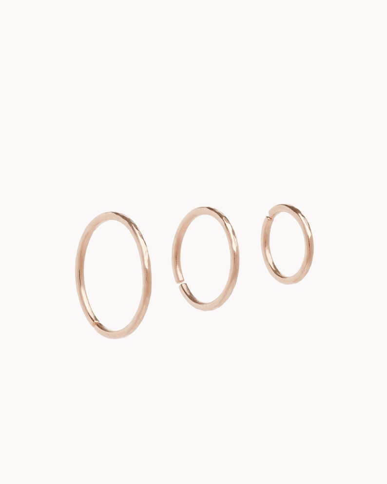 May include: Three gold hoop earrings of different sizes. The hoops are smooth and have a slightly hammered texture.