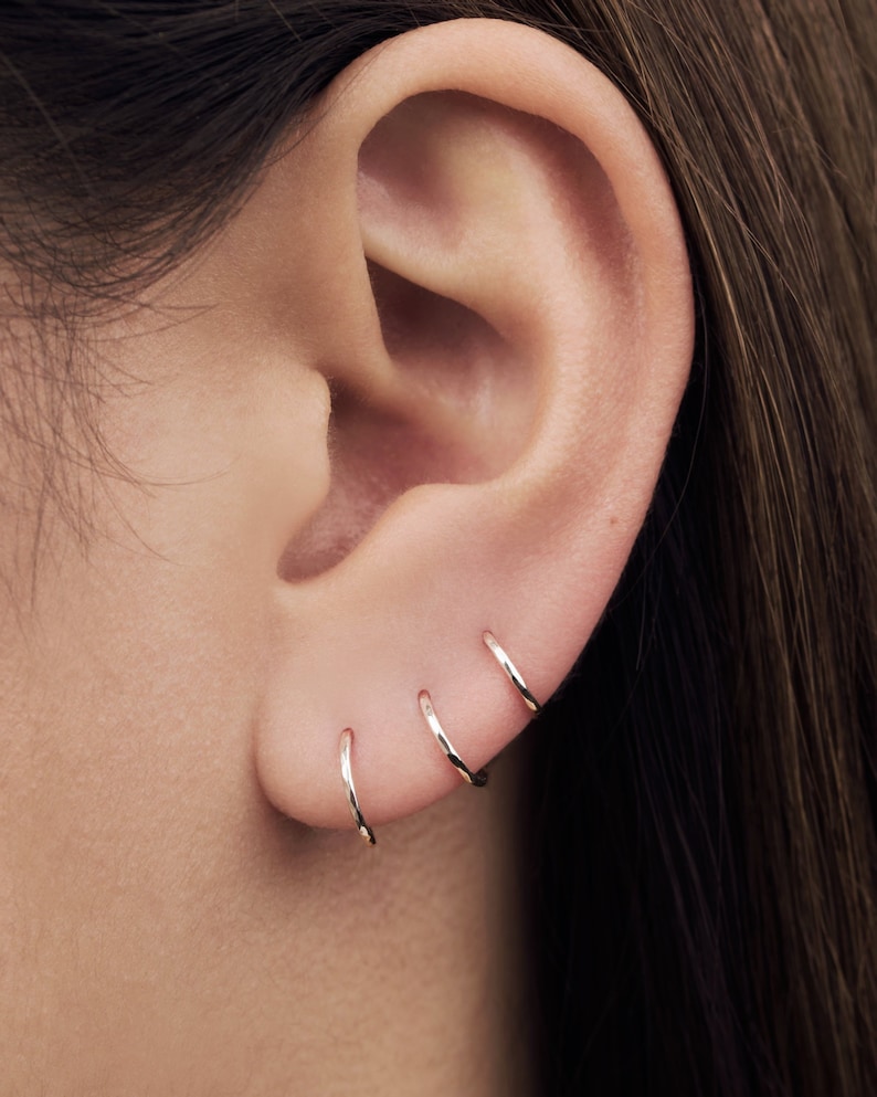 May include: Close-up of a person's ear with four gold hoop earrings. The earrings are different sizes and are worn in the upper lobe of the ear.