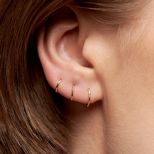 May include: Close-up of a person's ear with four gold hoop earrings. The earrings are different sizes and are worn in the upper lobe of the ear.