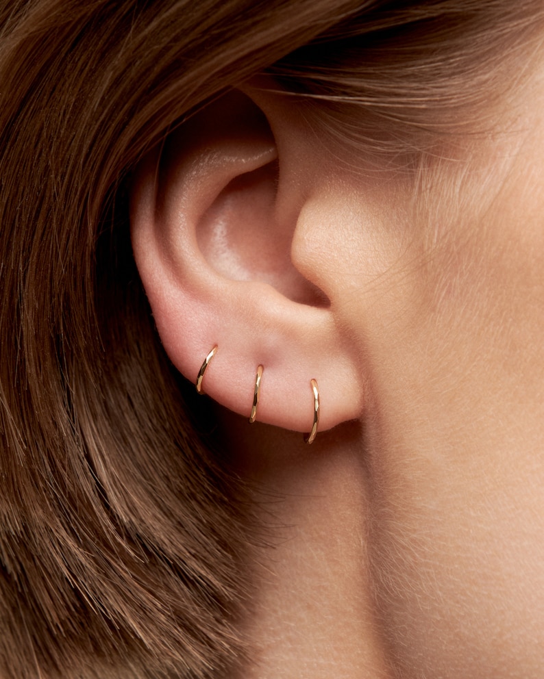 May include: Close-up of a person's ear with four gold hoop earrings. The earrings are different sizes and are worn in the upper lobe of the ear.