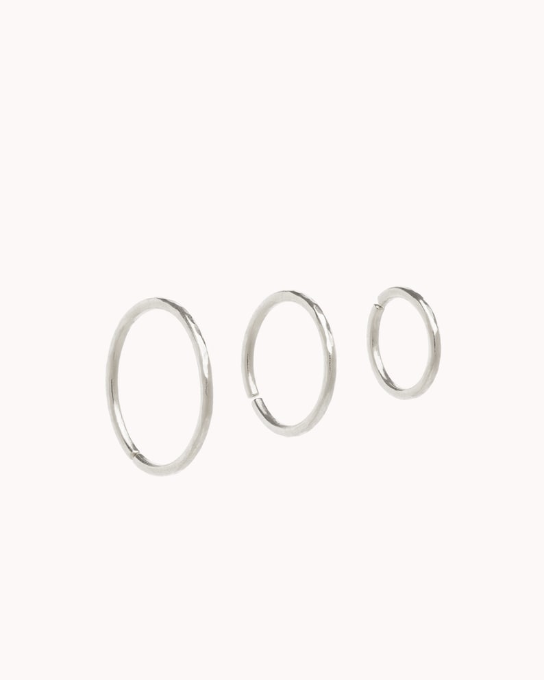 May include: Three silver hoop earrings of different sizes. The earrings are smooth and have a polished finish.