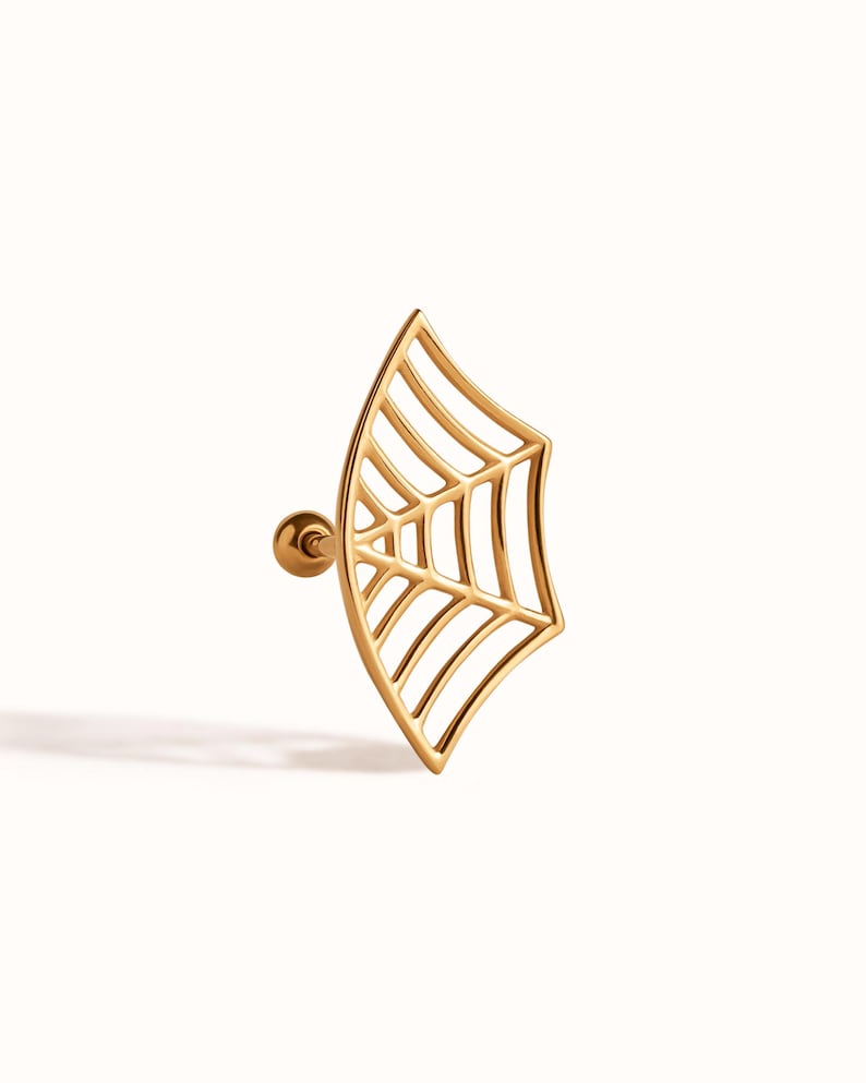 May include: A gold-toned ear stud featuring a flat, fan-shaped spider web design. The jewellery piece includes a thin, curved metal frame with internal web-like detailing and a small, round ball backing attached to a straight post for secure fastening.