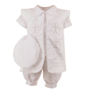 May include: White christening outfit for a baby boy, featuring a short-sleeved jacket with embroidered crosses, matching pants, and a white hat.