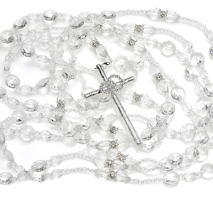 May include: A silver cross pendant hangs from a long strand of clear crystal beads. The beads are oval shaped and have a faceted finish.