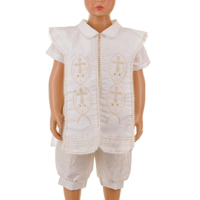 May include: White christening outfit with gold embroidered crosses on the front. The outfit includes a short-sleeved shirt and shorts.