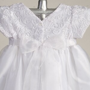 Pu&ograve; includere: Abito bianco per neonata con corpetto in raso e gonna in tulle. Il corpetto presenta delicati ricami floreali. L'abito ha una cintura in raso che si lega sul retro.