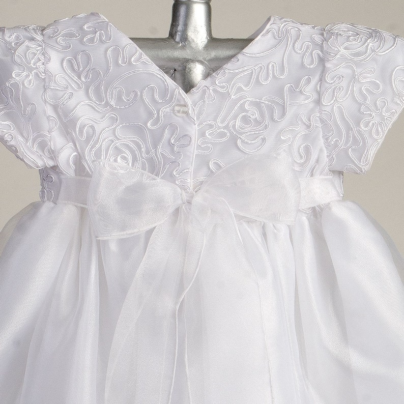 Pu&ograve; includere: Abito bianco per neonata con corpetto in raso e gonna in tulle. Il corpetto presenta delicati ricami floreali. L'abito ha una cintura in raso che si lega sul retro.