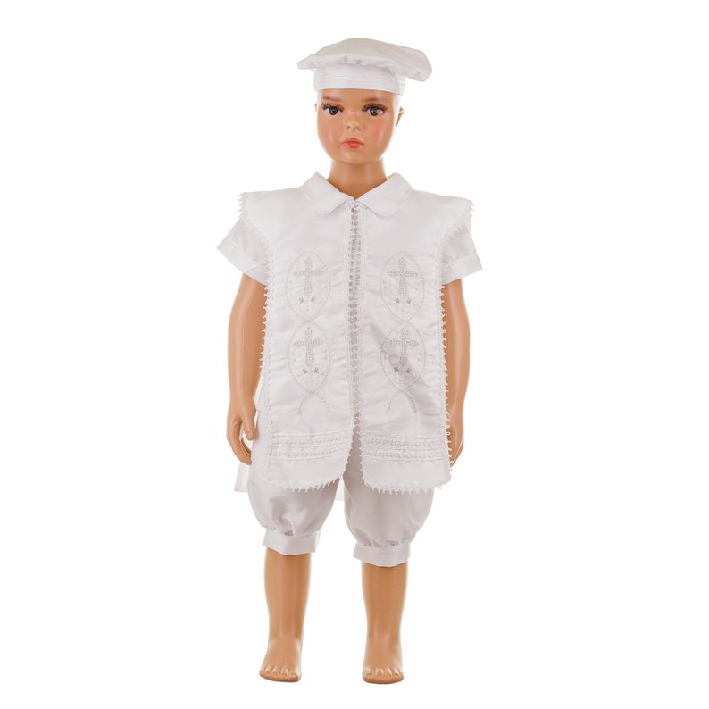 May include: White christening outfit for a baby or young child. The outfit includes a white vest with embroidered crosses, white shorts, and a white hat.