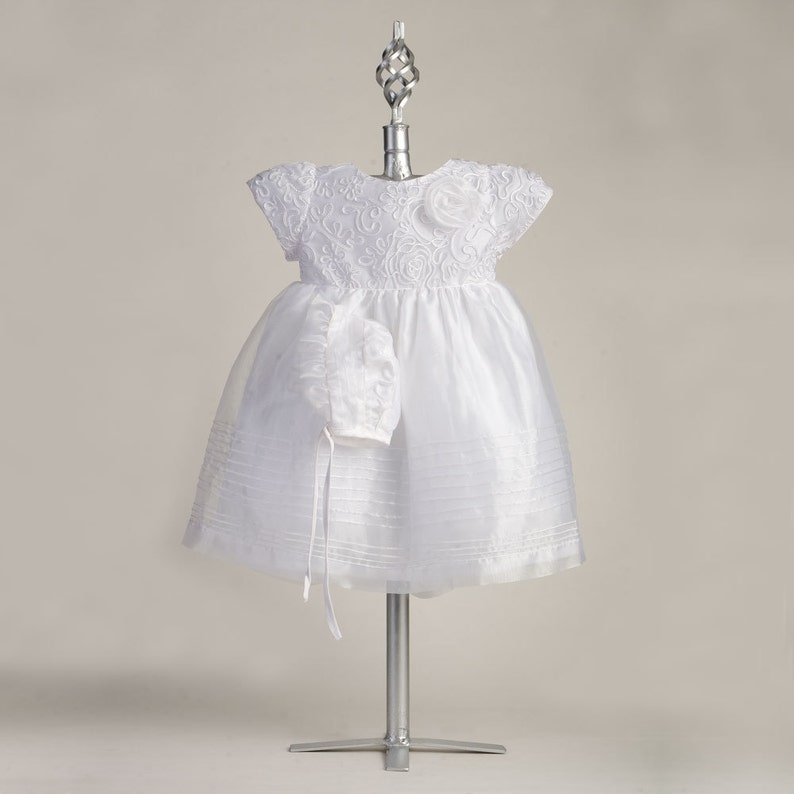 Pu&ograve; includere: Abito bianco per neonata con corpetto in pizzo e gonna in tulle. L'abito &egrave; abbinato a un berretto.