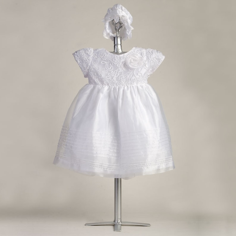 Pu&ograve; includere: Abito bianco per neonata con corpetto in pizzo e gonna in tulle. L'abito &egrave; abbinato a un cappello bianco.
