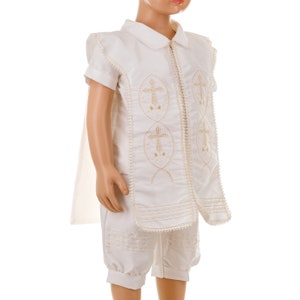 May include: White christening outfit for a baby or young child. The outfit includes a short-sleeved shirt with a collar, a pair of shorts, and a cape. The shirt and shorts have gold embroidered crosses.
