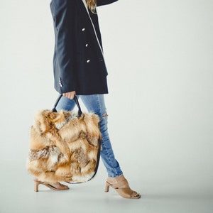 May include: A woman wearing a dark blue blazer, light blue jeans, and brown heeled sandals is holding a large, fluffy, brown and orange fur tote bag.