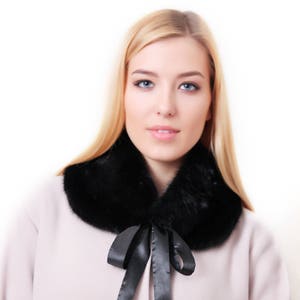 Puede incluir: Una mujer con un abrigo rosa claro con un cuello de piel negro y un lazo de sat&eacute;n negro.