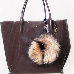 May include: A brown leather tote bag with a furry key chain. The bag has a shiny finish and a top handle.