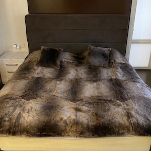 May include: A brown faux fur throw blanket on a bed with a brown headboard. The blanket is made of soft, plush fur and has a luxurious feel.