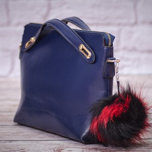 May include: A dark blue leather handbag with gold hardware and a black and red fur pom-pom keychain.