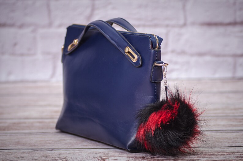 May include: A dark blue leather handbag with gold hardware and a black and red fur pom-pom keychain.