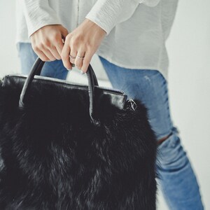 May include: A black faux fur handbag with a leather handle and zipper closure.