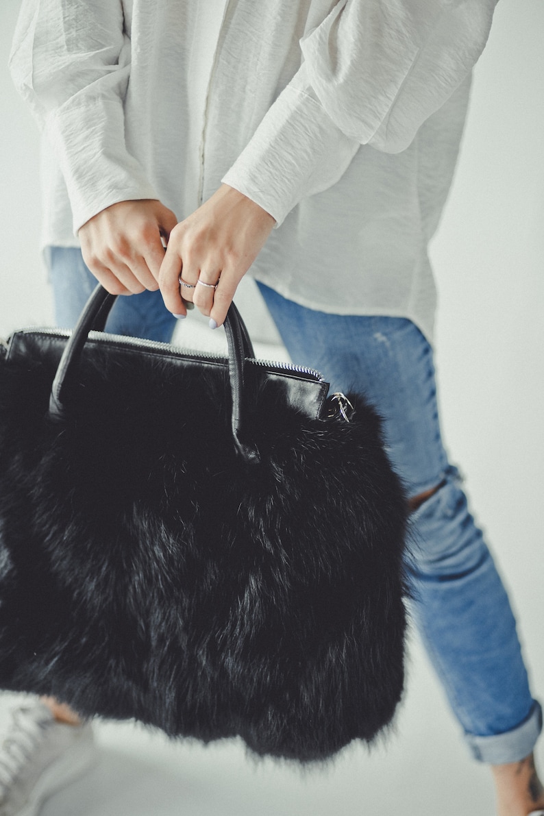 May include: A black faux fur handbag with a leather handle and zipper closure.