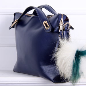 May include: A dark blue leather handbag with a gold zipper and a fluffy white and green fur keychain.