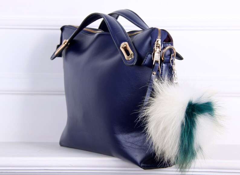 May include: A dark blue leather handbag with a gold zipper and a fluffy white and green fur keychain.