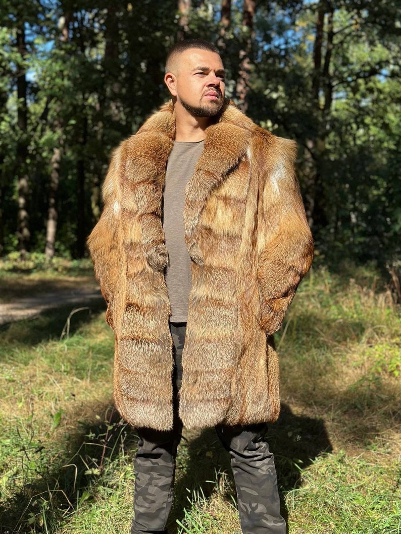 May include: A long, brown fur coat with a stand-up collar. The coat is made of fox fur and has a striped pattern. The person wearing the coat is standing in a forest.