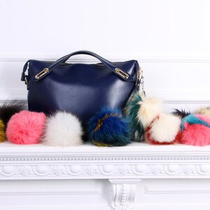 May include: A navy blue leather handbag with a gold chain and a variety of colorful faux fur pom-poms.