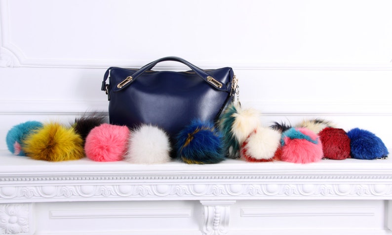 May include: A navy blue leather handbag with a gold chain and a variety of colorful faux fur pom-poms.