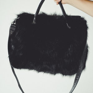 May include: A black faux fur handbag with a long black leather strap.