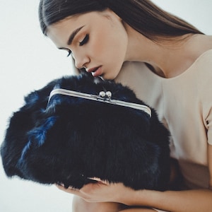 May include: A woman is holding a black faux fur clutch with a silver clasp. The clutch has a soft, fluffy texture.
