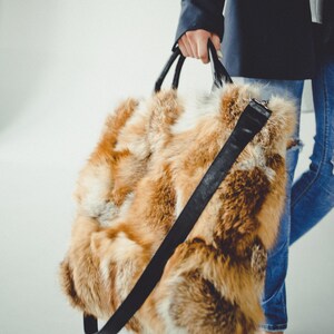 May include: A large, brown and white fur tote bag with a black leather strap. The bag is being held by a person wearing blue jeans and a dark blue blazer.