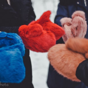 Op de afbeelding: Close-up van vier paar bontmutsen in verschillende kleuren: rood, blauw, roze en oranje. De mutsen zijn gemaakt van zacht, pluche bont en perfect om je handen warm te houden in de winter.