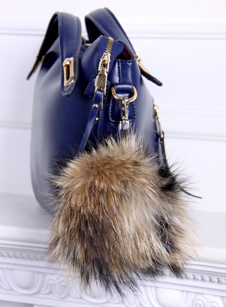 May include: A dark blue leather handbag with a gold zipper and a fluffy brown and black fur pom-pom keychain.