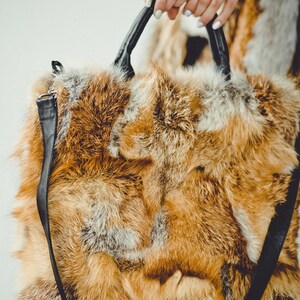 May include: A large, brown and white fur handbag with a black leather strap. The bag is made of fox fur.