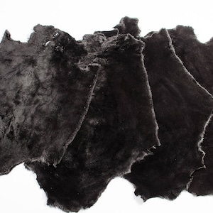 Könnte beinhalten: Ein Stapel dunkelbrauner Schaffellfelle. Die Felle sind weich und flauschig und haben ein natürliches, rustikales Aussehen.