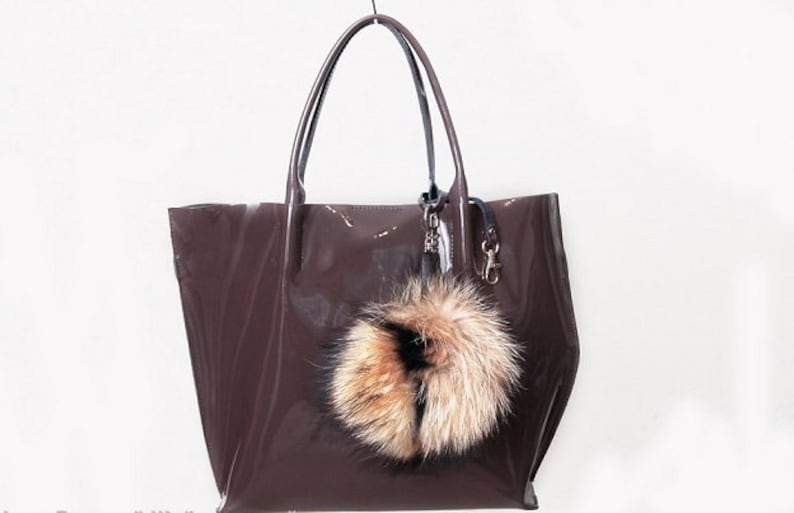 May include: A brown leather tote bag with a furry key chain. The bag has a shiny finish and a top handle.