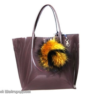May include: A brown patent leather tote bag with a large yellow and black fur pom-pom keychain.