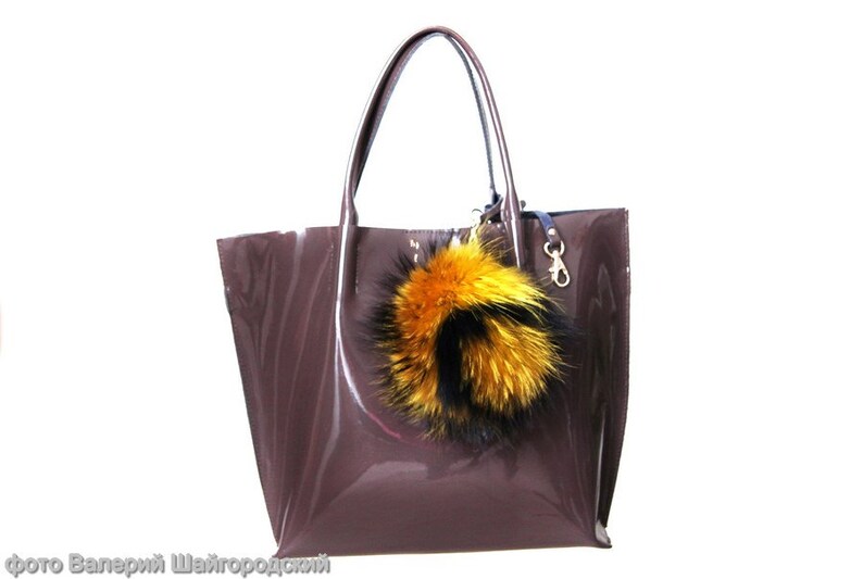 May include: A brown patent leather tote bag with a large yellow and black fur pom-pom keychain.