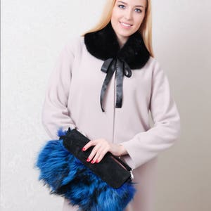 Puede incluir: Una mujer con un abrigo rosa claro con un cuello de piel negro y un bolso de mano de piel azul y negro.