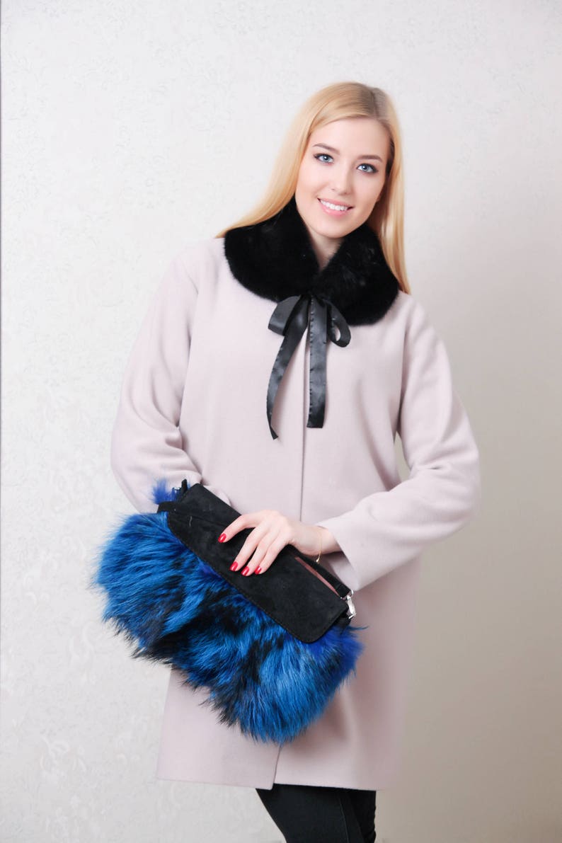 Puede incluir: Una mujer con un abrigo rosa claro con un cuello de piel negro y un bolso de mano de piel azul y negro.