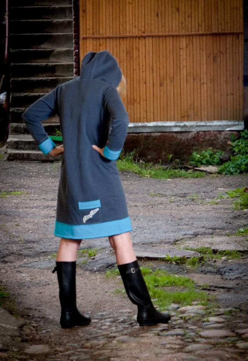 May include: A hooded dress with a blue trim and a small pocket on the front. The dress is made of a soft, dark gray fabric. The person is wearing black boots.