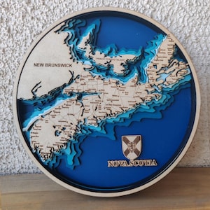 May include: A round, layered wooden map of Nova Scotia, Prince Edward Island, and New Brunswick. The map features a blue ocean and light brown landmasses with detailed city names. The words "NEW BRUNSWICK" and "NOVA SCOTIA" are visible.