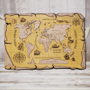 Puede incluir: Un mapa del mundo de madera con un aspecto envejecido. El mapa presenta continentes, océanos e ilustraciones de barcos, una rosa de los vientos y un sol. El texto incluye "Pacific Ocean", "Arctic Ocean", "Atlantic Ocean", "Indian Ocean" y "Antarctica".