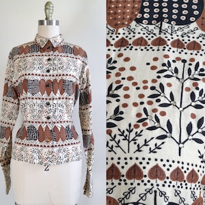 Puede incluir: Una camisa de manga larga con botones y un estampado geométrico marrón, blanco y negro. El estampado presenta árboles estilizados, hojas y corazones.