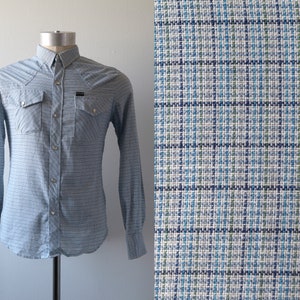 Op de afbeelding: Een lichtblauw, lang mouwig overhemd met knopen en een wit en blauw geruit patroon. Het overhemd heeft twee borstzakken met knoopsluiting en een enkele knoopsluiting aan de kraag.