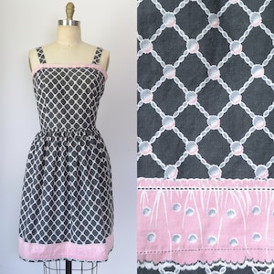 May include: A black and white patterned dress with a pink trim. The dress has a fitted bodice and a full skirt. The pattern is a geometric design with circles and lines.